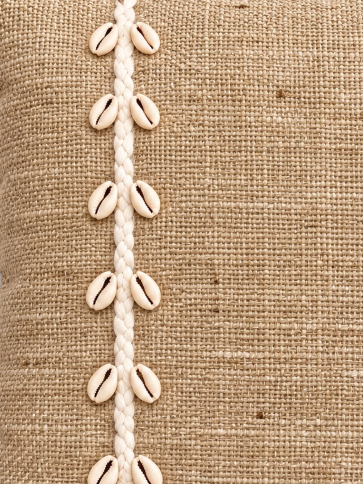 Détail des coquillages cauris et du tissage en jute beige du coussin carré balinais