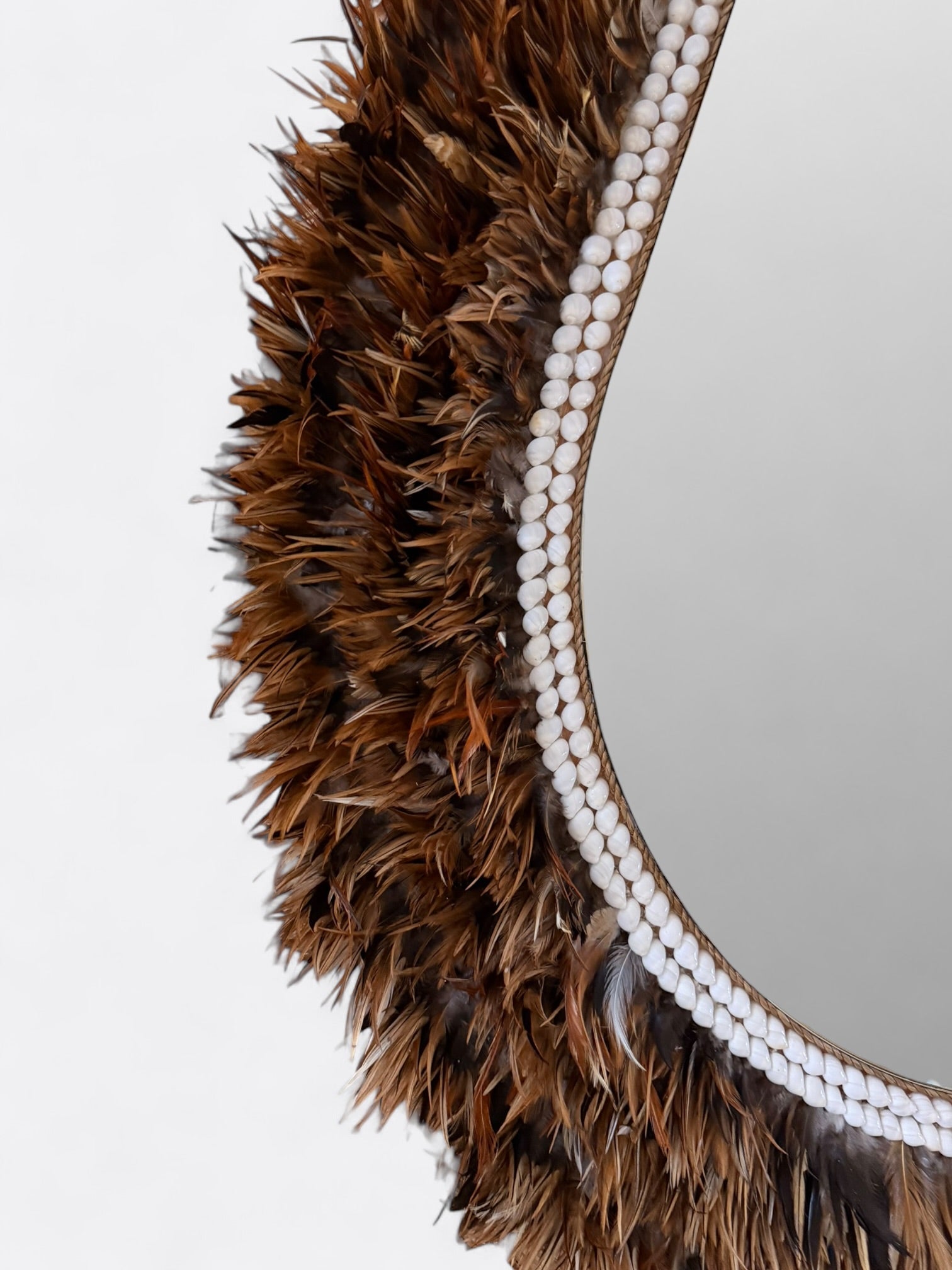 Détail des finitions artisanales, plumes et coquillages sur le cadre ovale du miroir Peniah