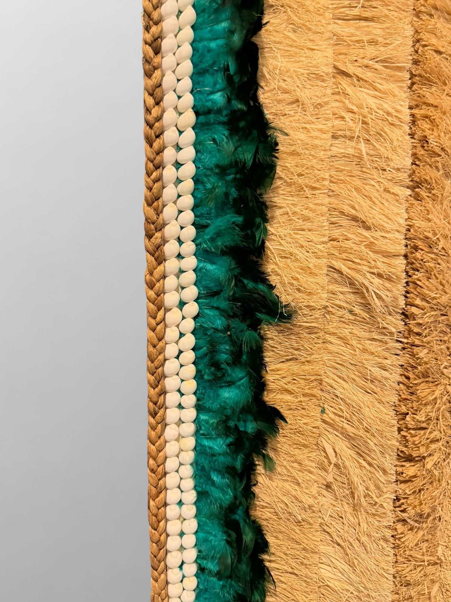 Gros plan sur le mélange de raphia tressé, plumes douces et coquillages du miroir artisanal Tahia